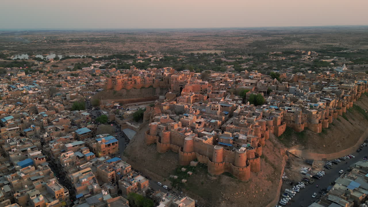 una toma de avión no tripulado en órbita del fuerte de jaisalmer al atardecer, con el fuerte dorado que se eleva sobre las casas circundantes y las carreteras sinuosas de jaisalmer, rajasthan india 4k