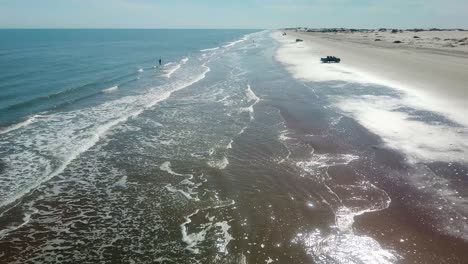 drone - rising, reveal view of the shoreline and surf at low tide on a gulf coast barrier island on a sunny afternoon, fisherman and vehicles in the distance - south padre island, texas