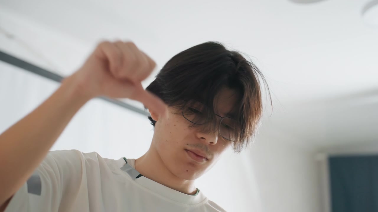 素早い身振り手振りをする若いアジア人男性。リラックスした環境での若いアジア人の日常ルーティン。柔らかな光が差し込む寝室で、日常の片付け中に素早い手の動きで作業するカジュアルな若いアジア人男性。