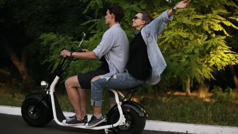 Ein-Glückliches-Paar,-Das-An-Einem-Sommertag-Auf-Einem-Elektrofahrrad-Auf-Der-Straße-Fährt.-Schönes-Mädchen-Und-Ihr-Freund-Genießen-Ihre-Zeit.-Parkgebiet