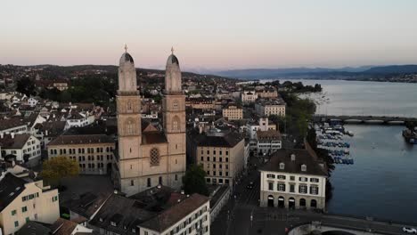 Aerial-view-of-Grossmünster-church-in-Zurich,-Switzerland-with-Lake-Zurich-in-the-background-at-dusk
