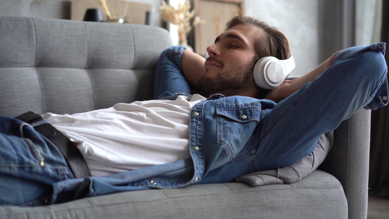 Giovane uomo rilassato sul divano mentre ascolta musica con le cuffie