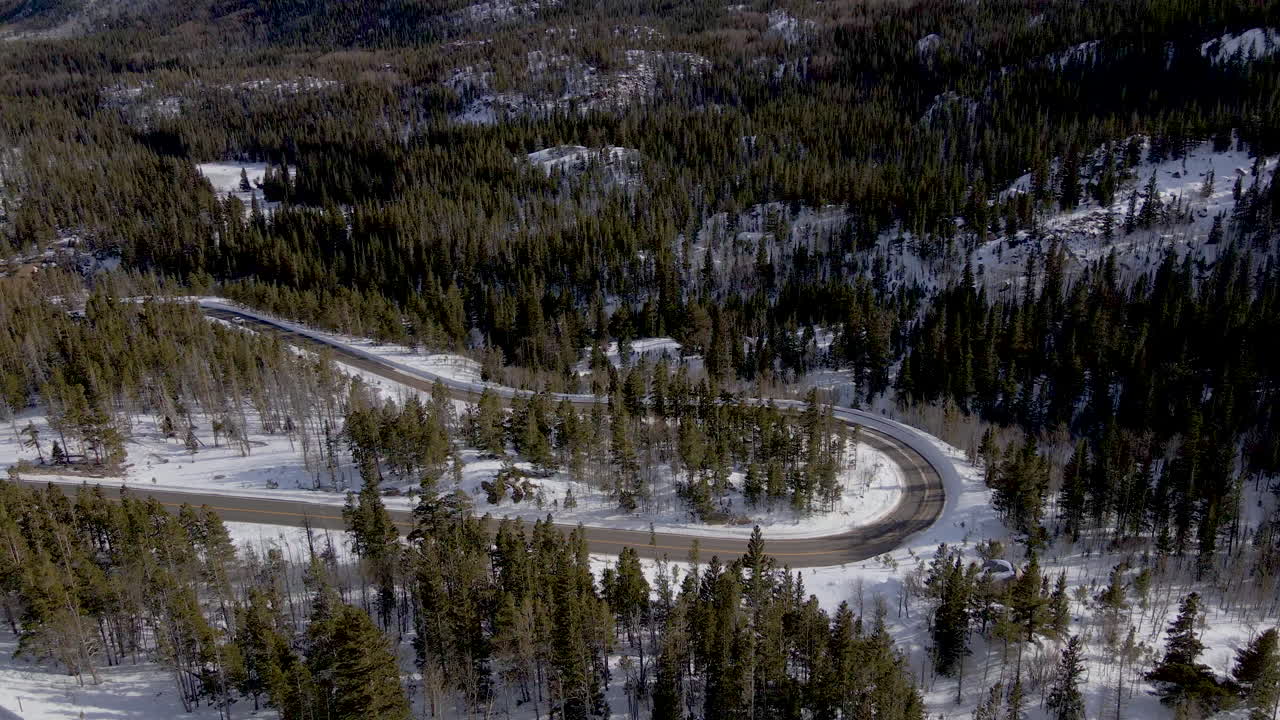 Winding high alpine hairpin turn in mountain road, snowy pine forest, aerial