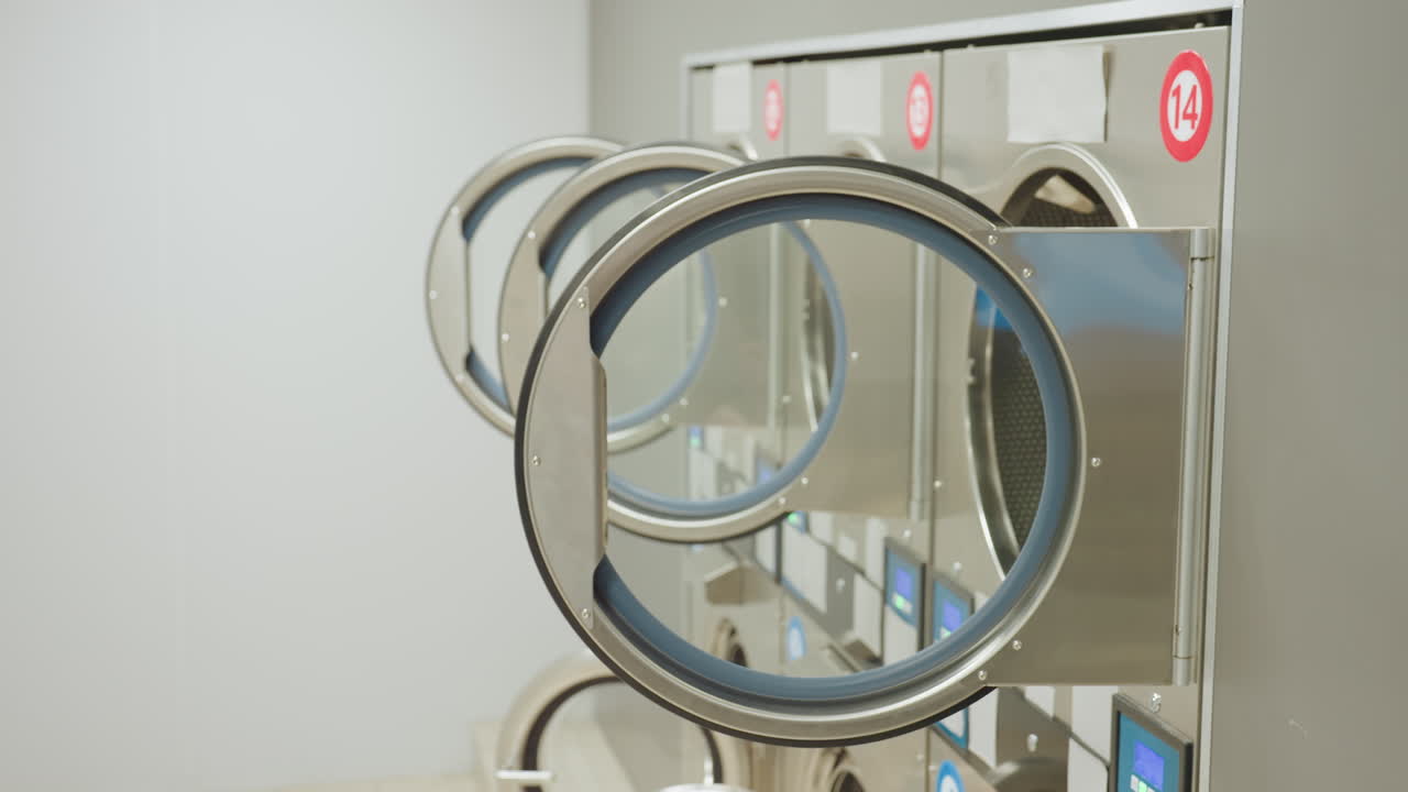 Close up view of tunnel washers with open circular doors in modern laundry facility as lights go off, highlighting stainless steel design, and reflective surfaces in clean environment