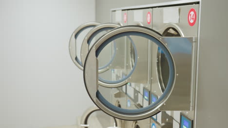 close up view of tunnel washers with open circular doors in modern laundry facility as lights go off, highlighting stainless steel design, and reflective surfaces in clean environment