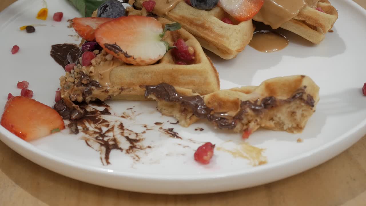 Plate of waffle topped with fresh fruit, chocolate spread, and syrup being cut into