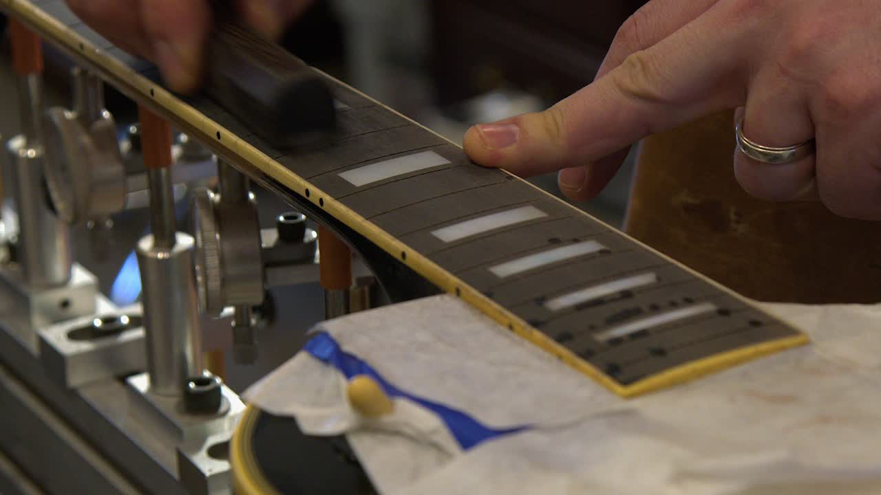 Técnico de guitarra en un taller de reparación rellena y lija diapasón de ébano en retrasteado.