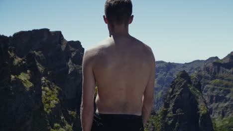 panning around shirtless man on overlook in dramatic mountains, slow motion