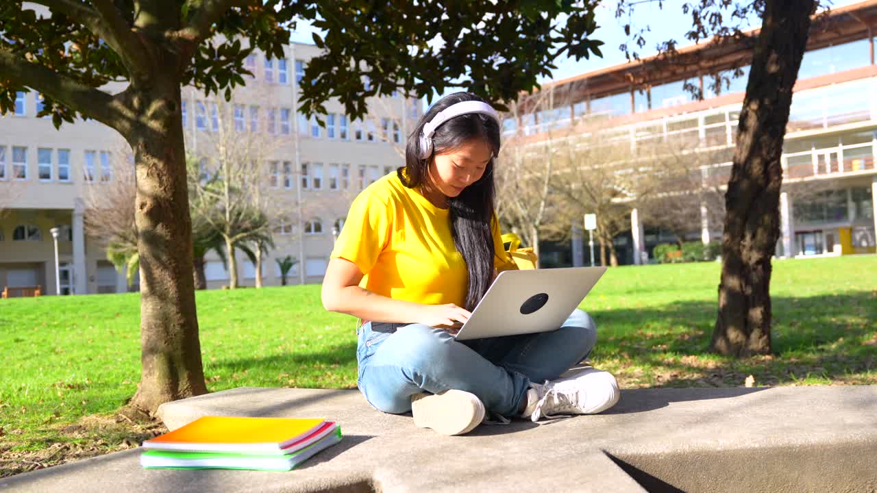Asian woman listening to music and working on her laptop outdoors