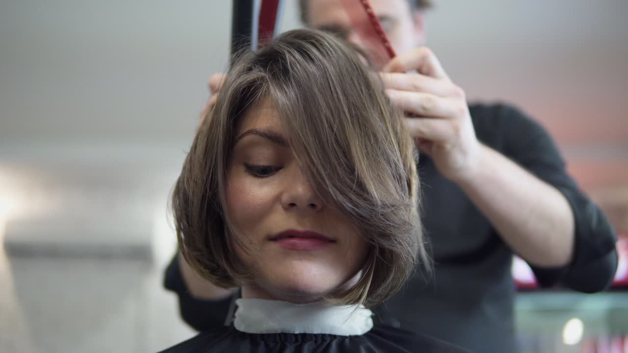 Hair stylist makes professional hairstyle of young woman in beauty studio. Hair straightening.