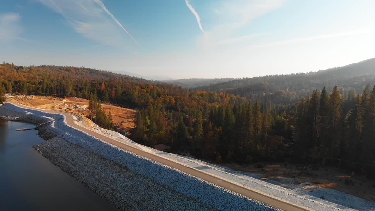 toma aérea de una presa en un lago alpino azul rodeado de pinos y montañas