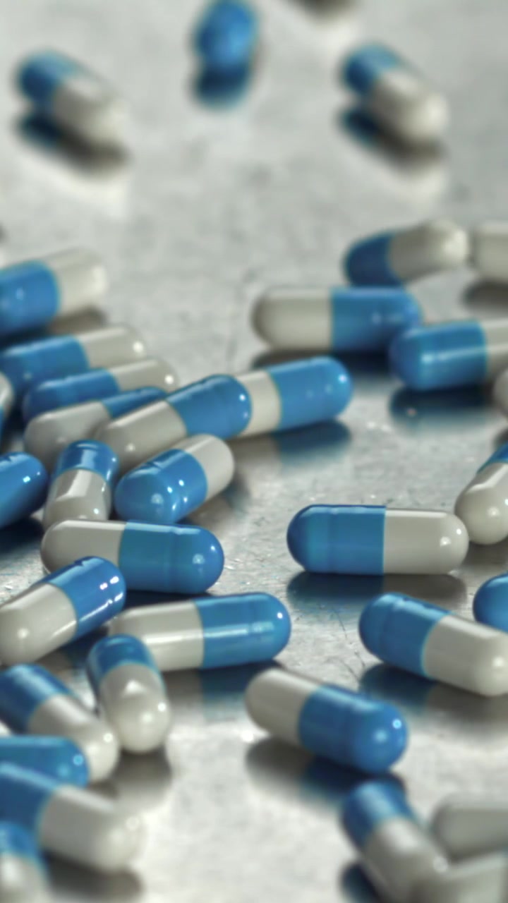 Capsule blu e bianche che cadono e rimbalzano su una superficie metallica.