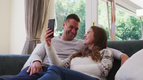 Pareja-Caucásica-Sonriendo-Mientras-Realiza-Una-Videollamada-En-Un-Teléfono-Inteligente-Sentado-En-El-Sofá-De-Casa