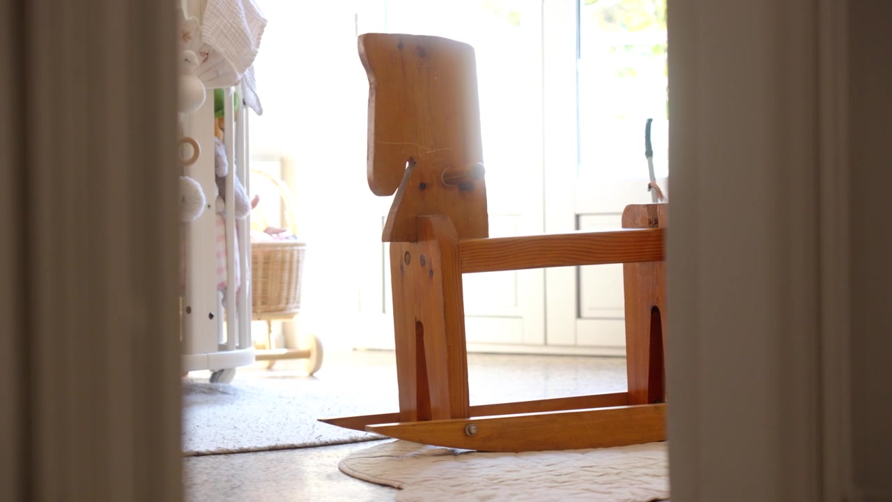 Wooden rocking horse and crib in softly lit nursery, viewed through doorway