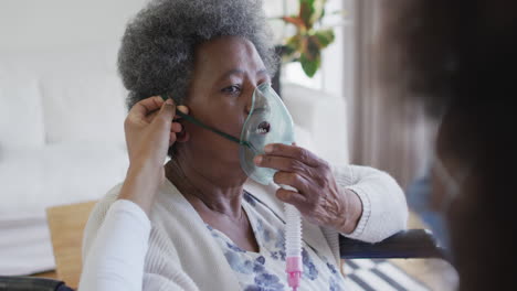 african american female doctor giving oxygen to senior female patient in wheelchair, slow motion