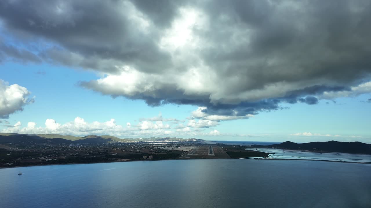 Pilot’s perspective POV FPV approaching to Ibiza’s airport as seen by the pilots of a jet from the cockpit overflying the Mediterranean Sea and flying under a layer of grey clouds, runway ahead. 4K