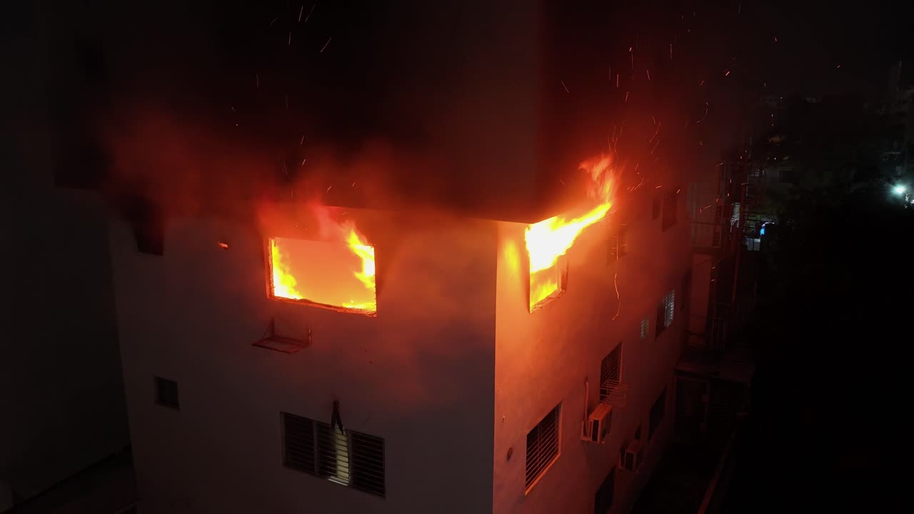 Aerial view of two windows with flames pouring out from inside a burning building