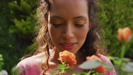 Portrait-of-happy-biracial-woman-smelling-roses-in-garden