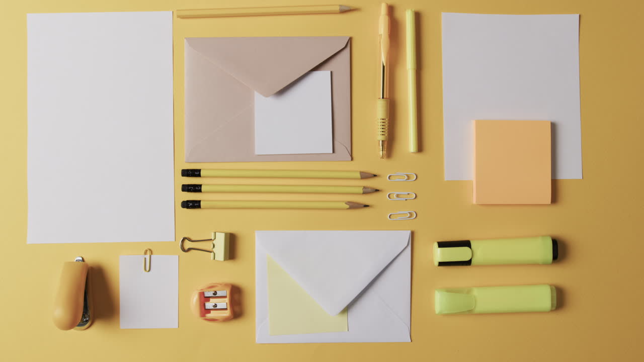 vista aérea de bolígrafos, lápices y artículos de papelería dispuestos sobre un fondo amarillo, en cámara lenta