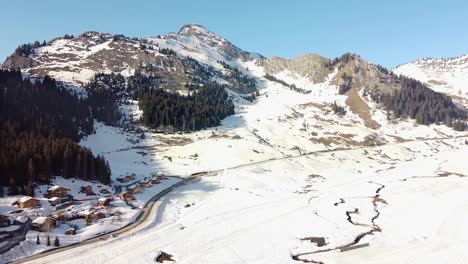 Tiro-De-Dron-De-Chalets-En-Las-Montañas-Alpinas-Francesas-Con-Una-Cumbre-Rocosa-Detrás