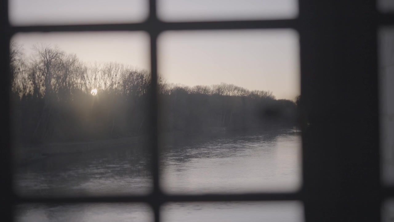 Solen står lavt over en rolig elv, dens glød diffundert gjennom et antikt vindu og reflekteres mykt på vannoverflaten i Paris