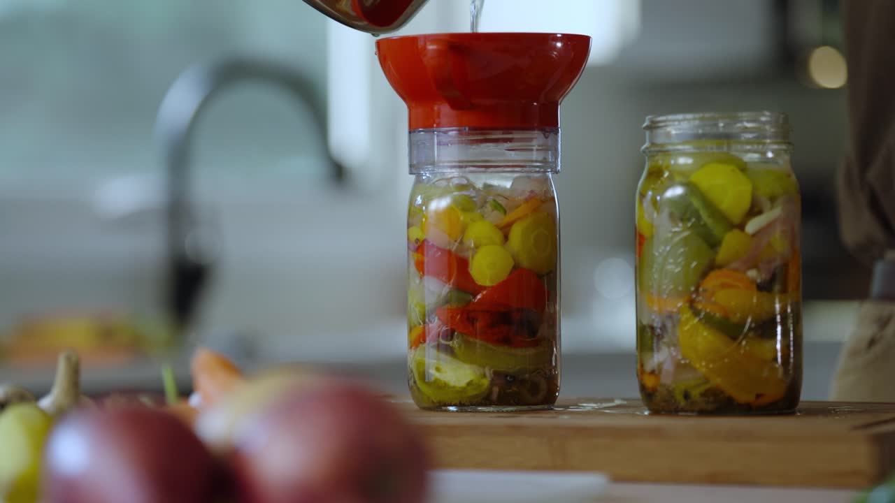 Pouring of hot water into glass jars containing pickled vegetables for preserving it for long time.