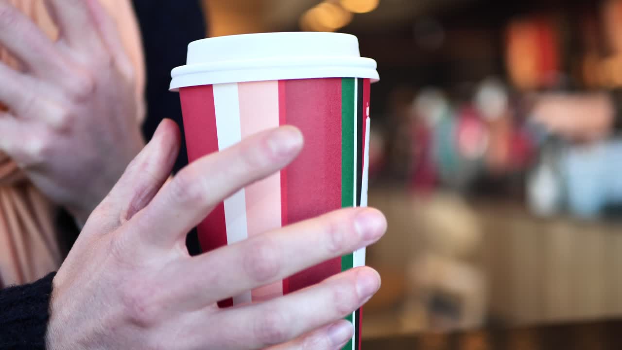Clip ripresa in una caffetteria con una donna caucasica che prende e poggia una tazza natalizia da caffetteria con caffè caldo o tè al suo interno.