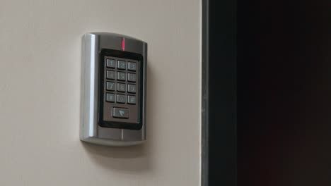 a man's holds a security card-faub up to a numeric keypad, which allows access to a locked door inside a secure business office