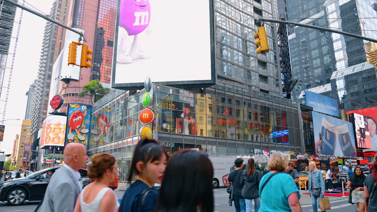New York, USA, 1 August 2025: Crowds of people walk by the street of New York, USA. Low angle view at the large screen on the building and numerous billboards