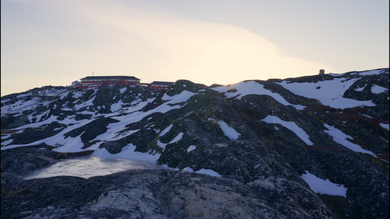 Sne og klipper ved kystlinjen, mens solen gløder over landskabet