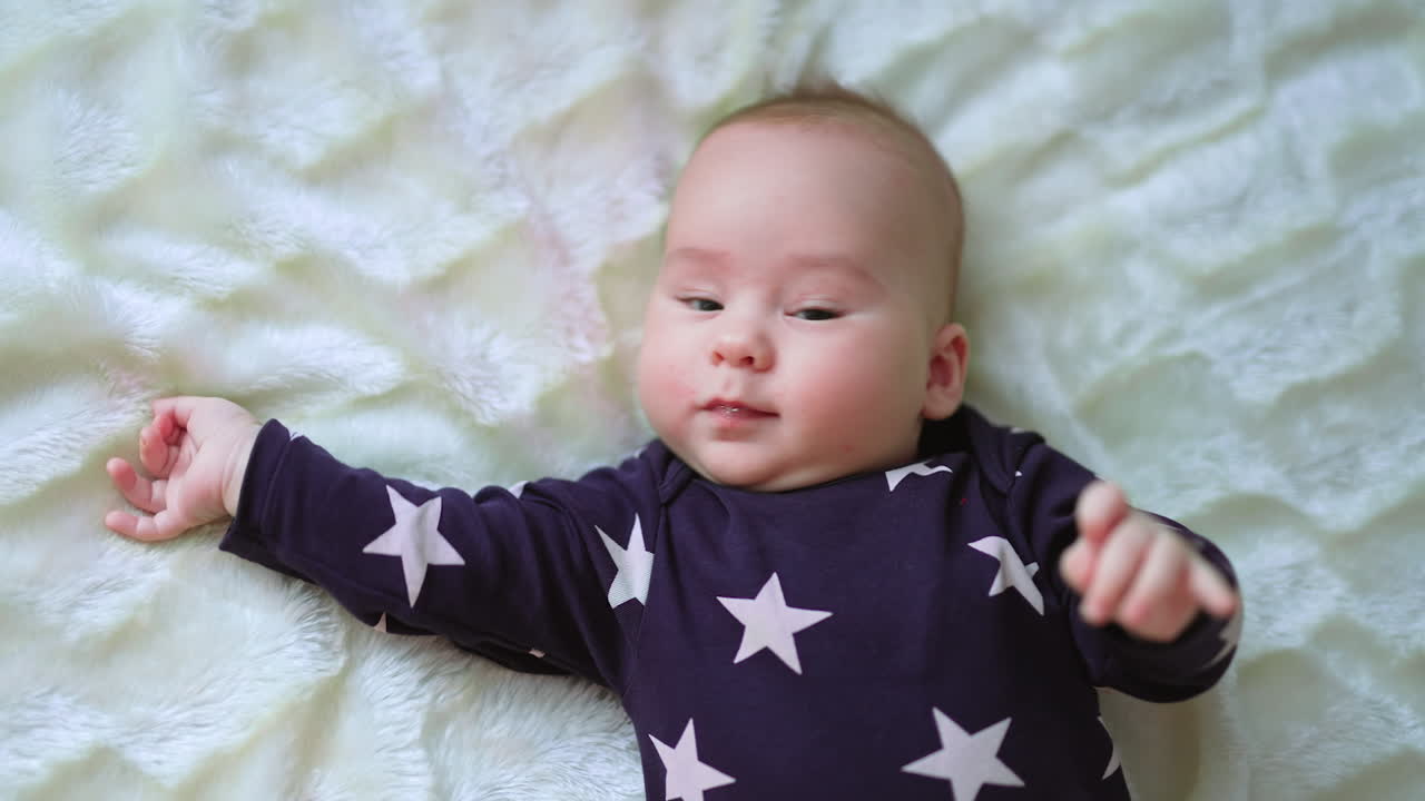 Smiling beautiful toddler being active on the bed. Top view on a nice cute cheerful baby on white backdrop.