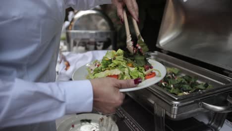 slow motion shot of a woman filling her plate up with a freshly prepared salad