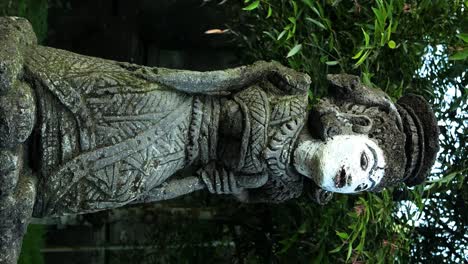 Toma-De-Paralaje-Vertical-De-Una-Estatua-Religiosa-En-El-Templo-Pura-Tirta-Empul-En-Bali-En-Indonesia-En-Ubud-En-Un-Hermoso-Jardín-Con-Vista-De-árboles-Y-Hojas-En-Cámara-Lenta