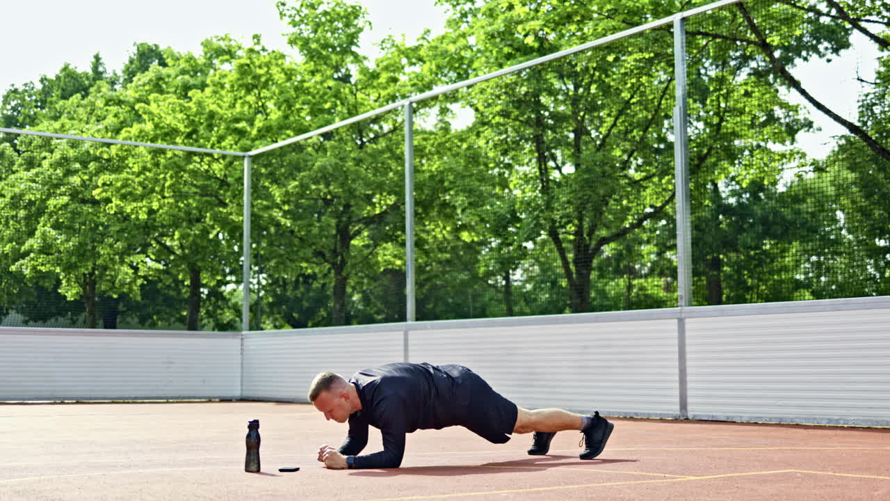 Hombre deportista en pantalón corto y camiseta. Hombre haciendo ejercicio matutino al aire libre y haciendo flexiones. Hombre deportista entrenando los músculos de los brazos en un campo deportivo. Concepto de estilo de vida activo.