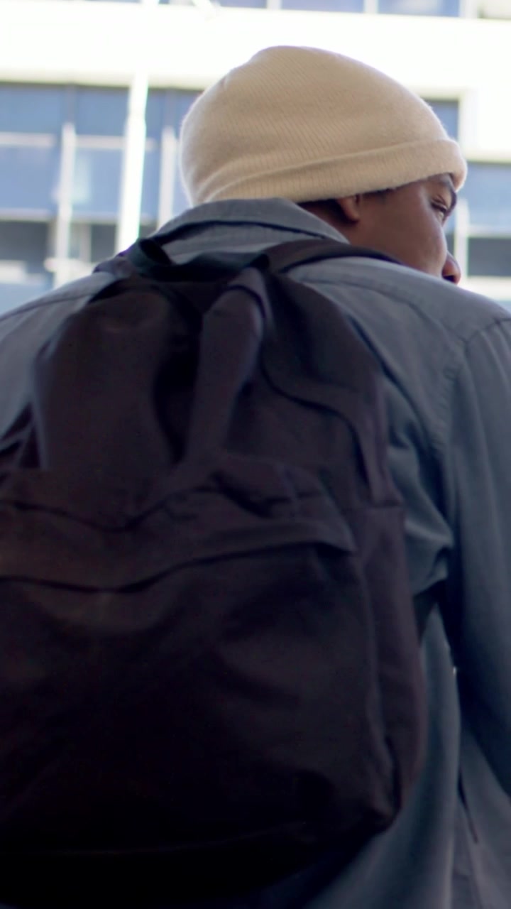 Vertical video: Camera recording man turning and scanning windows in lobby, beanie and backpack