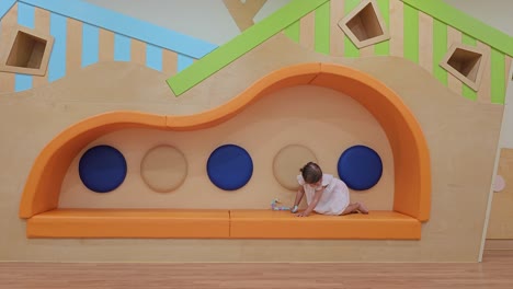 Happy-young-girl-crawling-back-and-forth-on-bench-at-indoor-child-play-area