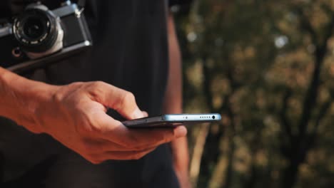 man using smartphone while holding vintage camera outdoors