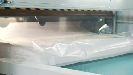 Close-up-of-a-factory-packaging-machine-wrapping-a-finished-mattress-in-stretch-film