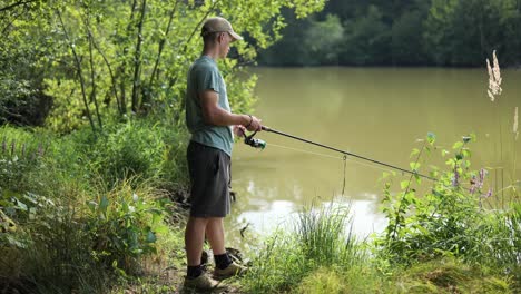 Junger-Männlicher-Angler-Dreht-Die-Winde-Der-Angelrute-Und-Wickelt-Die-Leine-Auf-Dem-Trüben,-Trüben-See-Ein