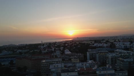 Ascending-drone-shot-showing-golden-sunset-over-Lisbon-City-and-Rio-Tejo,-Portugal