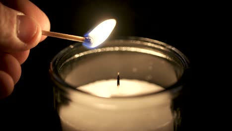 Slow motion macro footage of a white candle lit by a match on a dark background