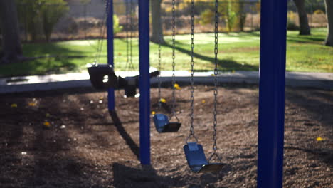 Panning from the sun and trees down to a kids park playground with an empty swing set