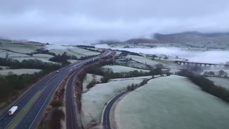 Leichter-Verkehr-Auf-Der-Autobahn-M6-Mit-Niedriger-Wolkendecke-Auf-Hügeln-An-Frostigen-Wintermorgen-Und-Steinviadukt-Im-Hintergrund-Von-Dunst-Und-Nebel