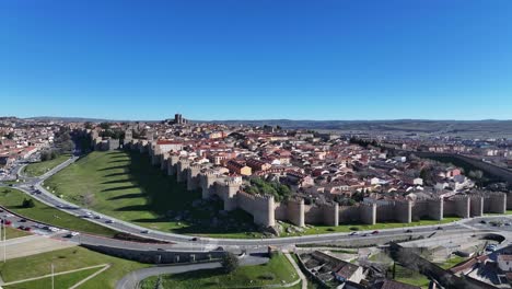 hover-flight-with-drone-viewing-the-medieval-walled-city-of-Avila-World-Heritage-Site-of-Avila-focused-on-the-road-with-cars-driving-on-a-sunny-morning-with-a-blue-sky-Avila-Spain