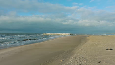 Aerial establishing view of protective stone pier with concrete blocks and rocks at Baltic sea coastline at Liepaja, Latvia, strengthening beach against coastal erosion, drone shot moving forward low