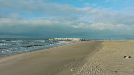 aerial establishing view of protective stone pier with concrete blocks and rocks at baltic sea coastline at liepaja, latvia, strengthening beach against coastal erosion, drone shot moving forward low