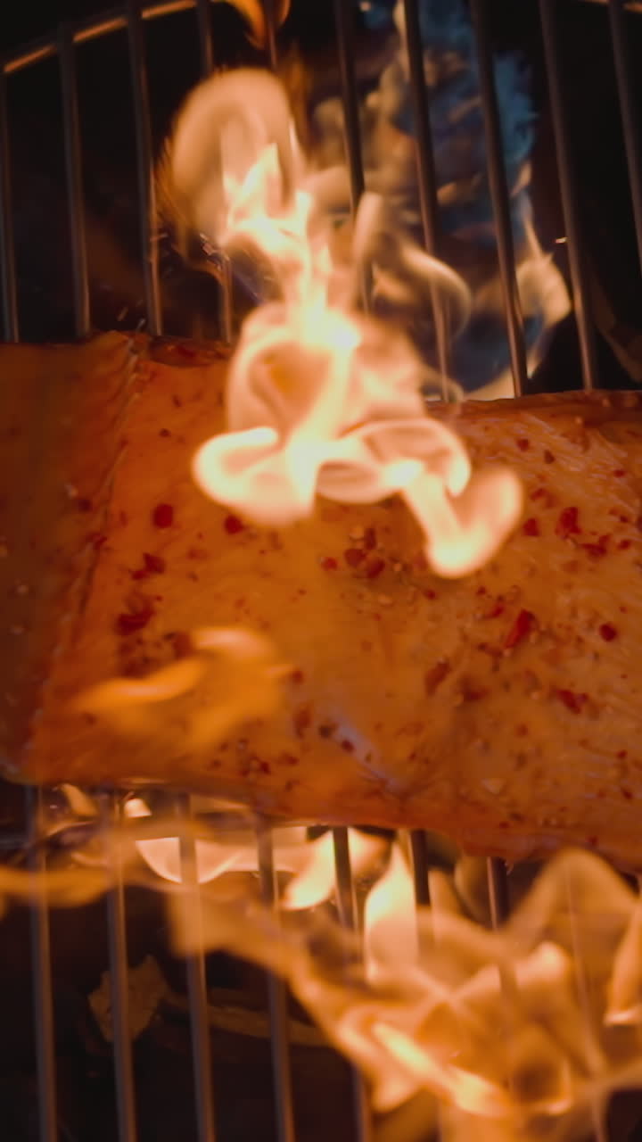 Cooking delicatessen trout red fish with open bright burning fire on brazier with grid and charcoals at darkness close view slow motion