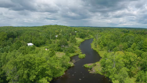 Vista-Por-Drones-De-Un-Río-Con-Cabañas-A-Lo-Largo-De-La-Orilla-En-Un-Día-Nublado