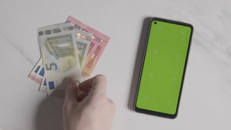 Overhead-Währungsaufnahme-Person,-Die-Euro-Banknoten-Und--Münzen-Zählt,-Neben-Greenscreen-Handy-1