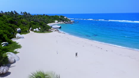 Flying-over-palm-trees-unveiling-the-white-sanded-Beach-of-Tayrona-national-park-in-Santa-Marta,-Colombia